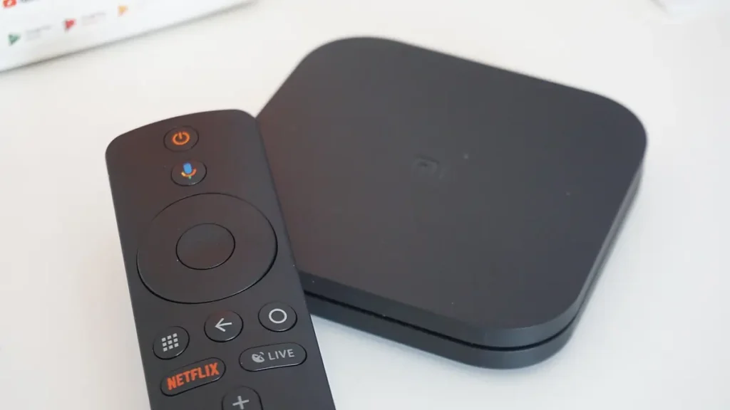 Black Android TV box beside its remote control with Google Assistant and live TV buttons