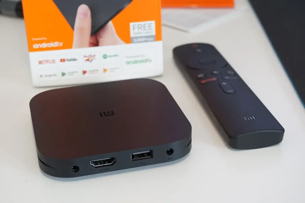 Android TV box with its retail packaging and remote, showing HDMI and USB ports on the rear panel