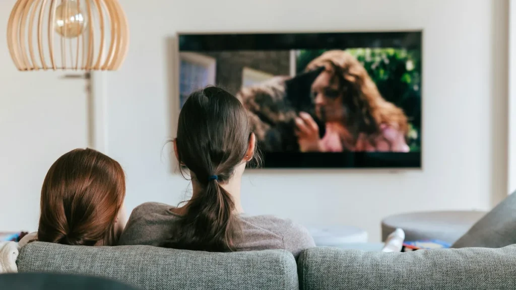 Two people on a sofa watching a large wall-mounted smart TV in a bright modern living room