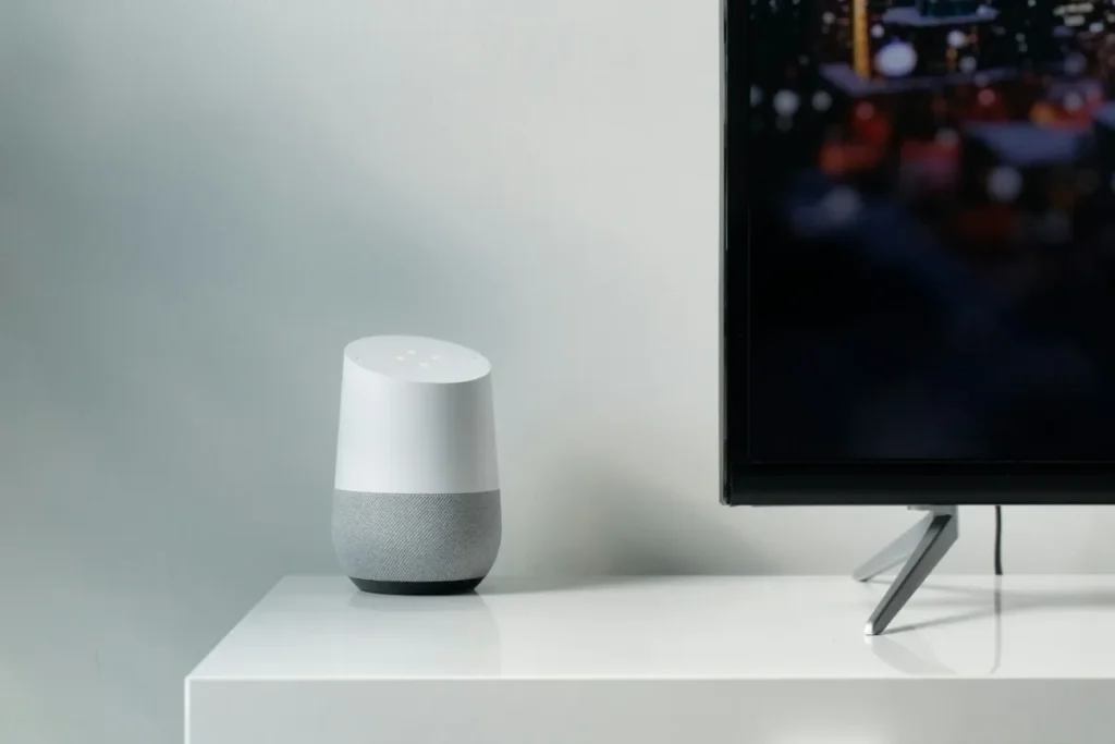 Google Home smart speaker on a white TV unit beside a flat-screen television, the kind of Google Home setup a Chromecast joins