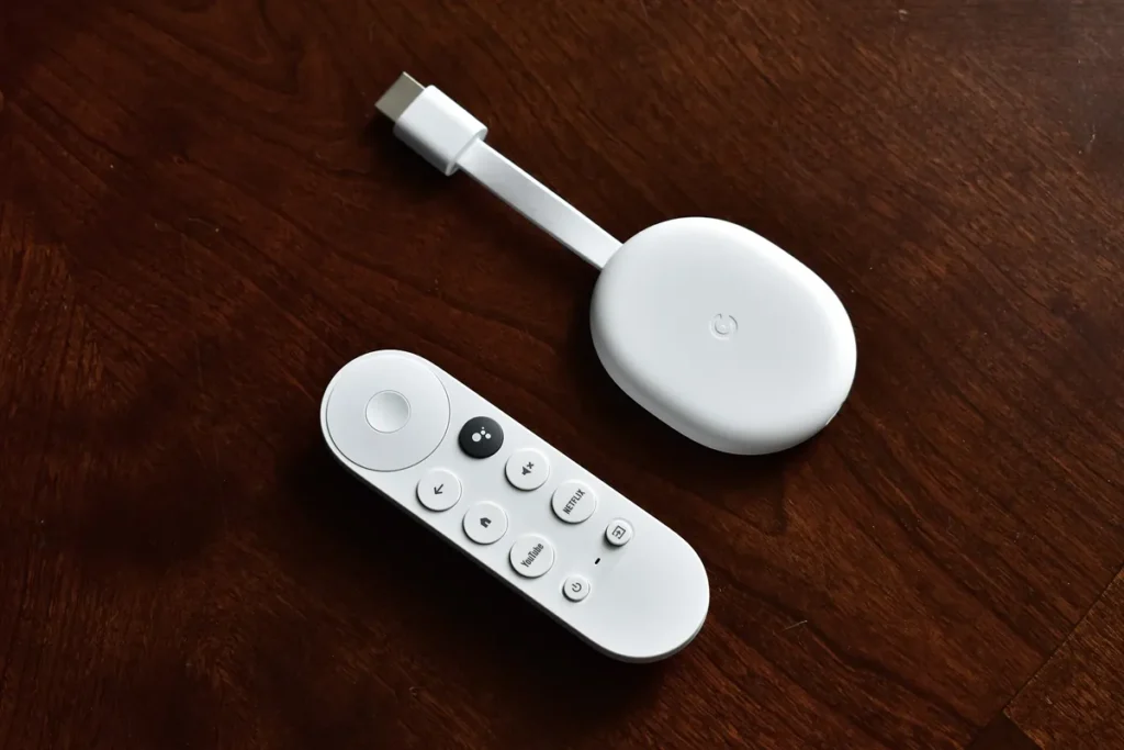 A white Chromecast with Google TV streaming device and its remote on a wooden table