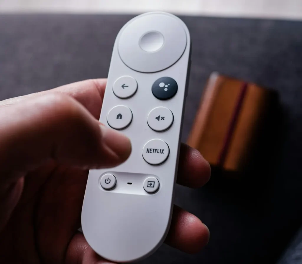 Hand holding a Google TV remote with direction pad, home and back buttons used to set up an Android TV box
