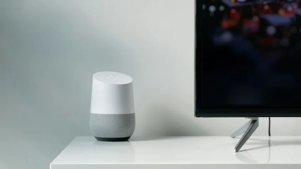 Google Home smart speaker on a white TV unit beside a television, the kind of Google Home setup the Google TV Streamer 4K can act as a hub for
