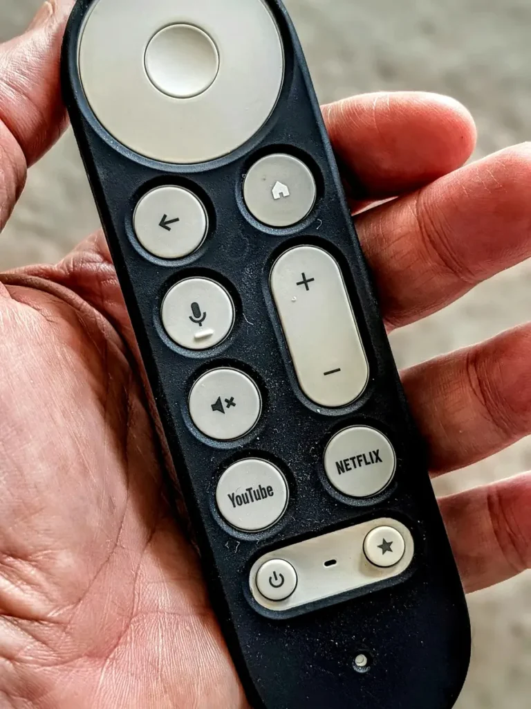 Hand holding the Google TV Streamer 4K Voice Remote, showing the circular pad, voice button and the customisable star button