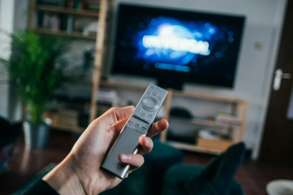 Hand holding a TV remote pointed at a television in a living room, the way Kodi on Firestick is navigated