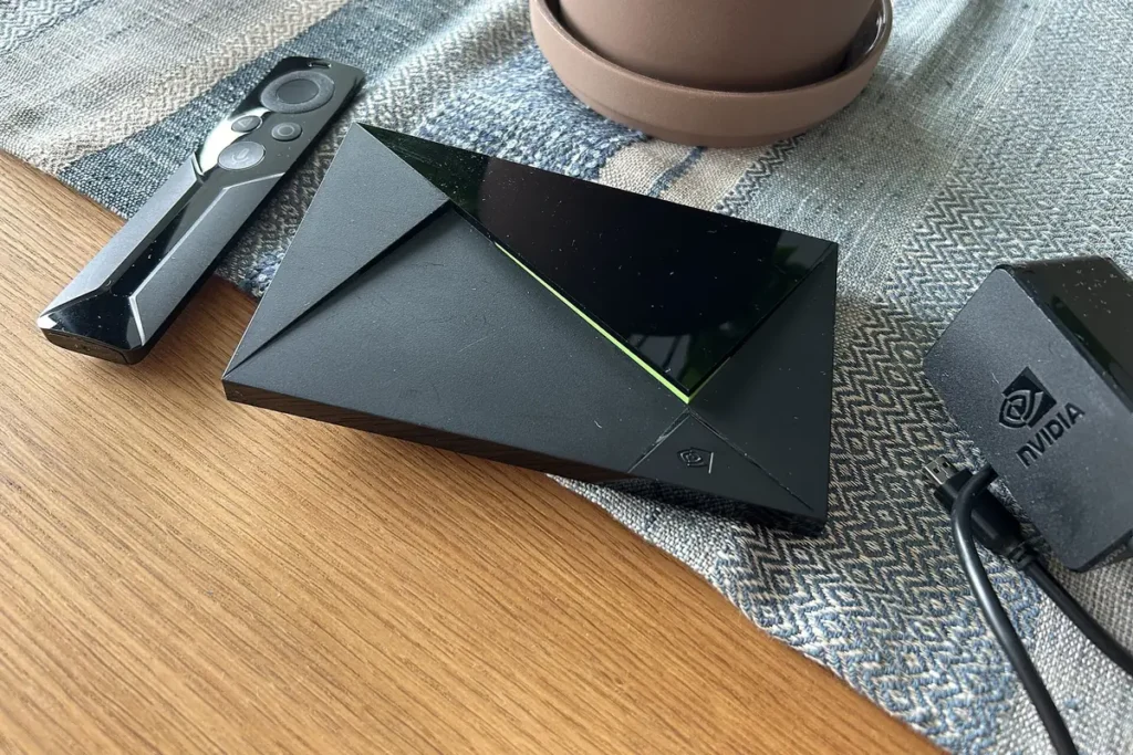 NVIDIA Shield TV streaming box beside its remote control and power adapter
