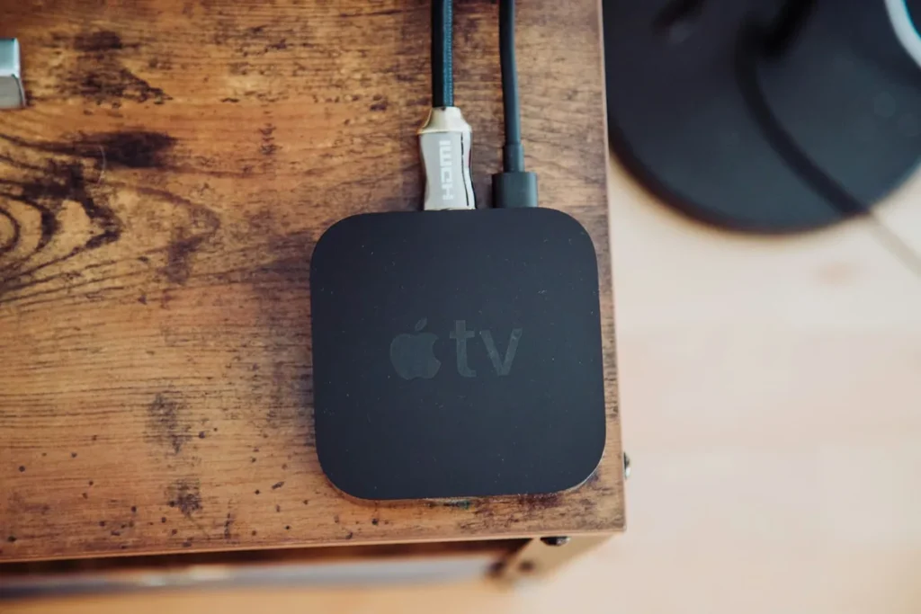 Apple TV smart TV box on a wooden table with an HDMI cable and power lead connected